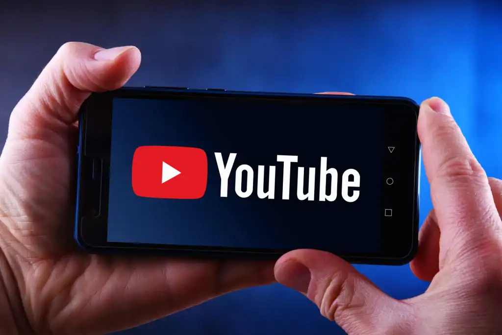 Persona sosteniendo un móvil con el logo de YouTube en pantalla, simbolizando cómo crear un tráiler de canal en YouTube